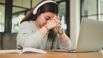 Young asian girl holding hands and head down tired expression while studying online with laptop. / Photodune, Misc