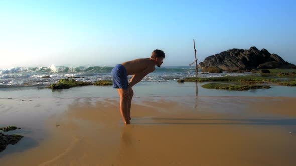 Sporty Athlete Stands on Wet Sandy Beach with Hands on Knees