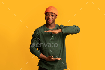 Object With His Hands, Happy Black Man Holding Something In Arms While Standing Isolated On Yellow Background, Recommending New Item, Copy Space