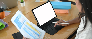 A woman is using a computer tablet with a white blank screen at the wooden working desk. / Photodune, Misc