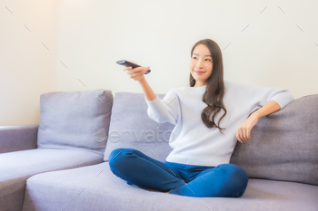 Portrait beautiful young asian woman use remote for change channel / Photodune, Misc