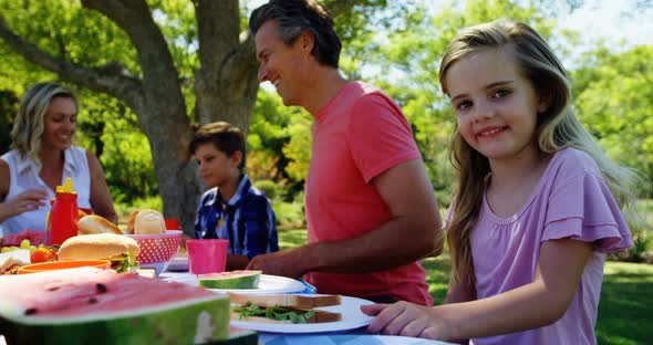 Girl sitting at the table and having meal with her family in park 4k