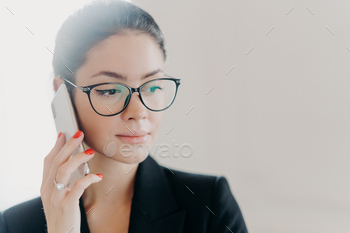 化粧をした深刻なブルネットの女性マネージャーは、流行の眼鏡をかけ、ビジネスパートナーを呼び出します / Photodune, Misc