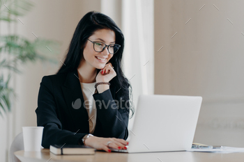 Cheerful female employee types on laptop computer, works remotely, concentrated with smile at laptop / Photodune, Misc