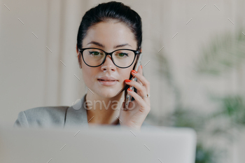Serious woman talks via mobile phone, concentrated into screen, calls business partner / Photodune, Misc