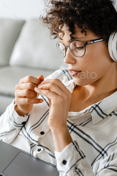 Young curly woman in headphones using laptop while sitting on armchair / Photodune, Misc