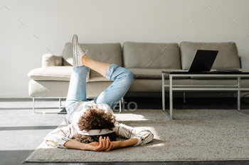 Young curly woman listening music with headphones while lying on floor / Photodune, Misc