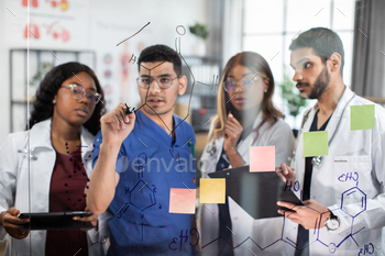 Team of doctors, discussing in front of glass wall, writing formulas, using notes and stickers / Photodune, Misc