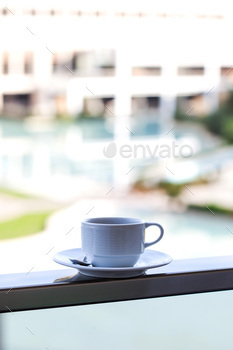 White mug on a white saucer with coffee on the outdoor pool on site. / Photodune, Misc