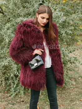 air and makeup posing in marsala lama fur coat at park. City fashion. Trendy girl