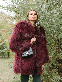 air and makeup posing in marsala lama fur coat at park. City fashion. Trendy girl