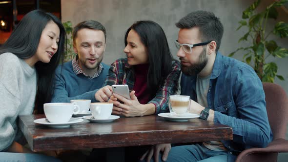 Joyful Young People Chatting and Laughing Having Fun Using Smartphone in Cafe