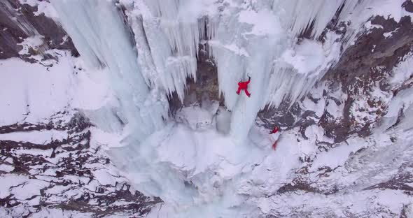 Aerial drone view of a man ice climbing on a frozen waterfall in the mountains.