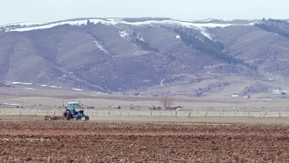 Spring in Wyoming as farmer plows field with tractor and snow on the hilltops