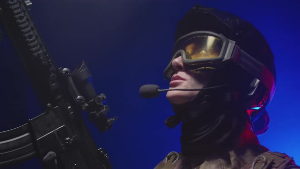 Woman Soldier in Helmet Glasses and Headset Reports on the Radio Looking Around Holding a Rifle and