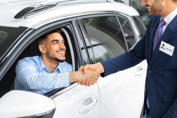 Happy middle-eastern man sitting in car shaking sales manager hand / Photodune, Misc