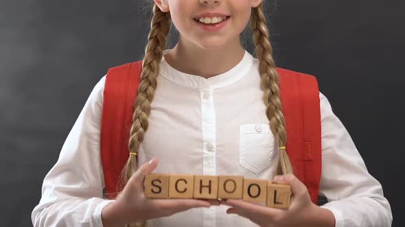 Nice Little Girl Holding Wooden Cubes With School Word Against Blackboard