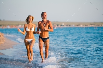 Beautiful young couple runnung at sea water edge and holding hands / Photodune, Misc