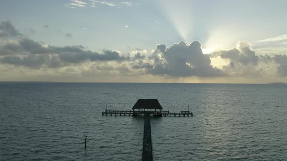 Aerial drone tilt up shot of sun rays through clouds over wooden pier on sea water in Mexico, North