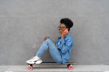 Happy trendy black girl talk on phone. Stylish african woman in urban denim outfit calling on cell / Photodune, Misc