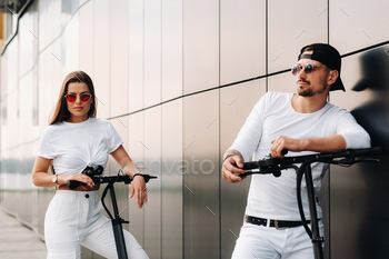A girl and a guy are walking on electric scooters around the city, a couple in love on scooters / Photodune, Misc