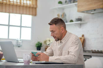 Good-looking bearded man sitting in the kitchen and typing a message / Photodune, Misc