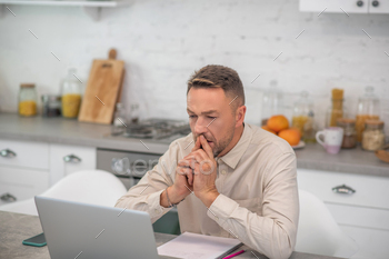 Good-looking bearded man sitting in the kitchen and working on laptop / Photodune, Misc