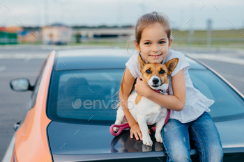 Girl with appealing appearance, hugs her favourite pet, have journey together with parents by car / Photodune, Misc