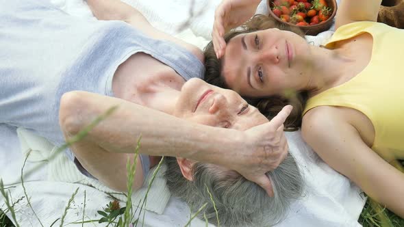 Beautiful Old Grandmother with Grey Hair and Face with Wrinkles is Lying on White Carpet with Her