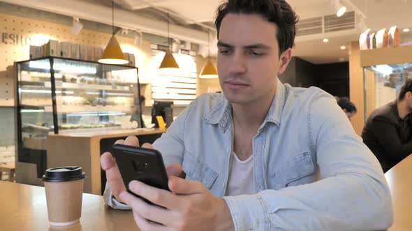Shocked Young Man Wondering While Using Smartphone in Cafe