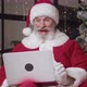 Happy Cheerful Goodnatured Elderly Bearded Man in Santa Claus Carnival Costume Using Laptop While - VideoHive Item for Sale