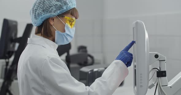 Female Young Researcher in Protective Mask and Yellow Googles Working on Computer