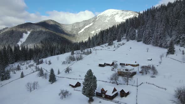 Aerial winter landscape with small rural houses between snow covered forest in cold mountains. alt