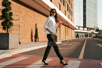 Woman in white shirt holding a coffee to go crossing the street / Photodune, Misc