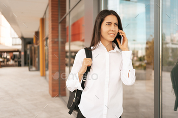 Woman with business backpak walking while speaking on the phone near a a business building / Photodune, Misc