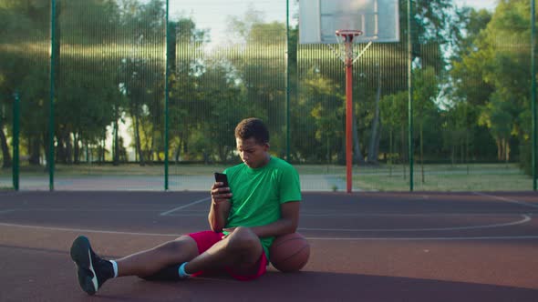 Basketball Player with Phone Relaxing on Outdoor Court