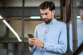 Young bearded man in a blue shirt holding the phone and typing a message / Photodune, Misc