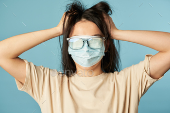 ask and glasses on her eyes on a blue background. Copy space. Quarantine, epidemic concept