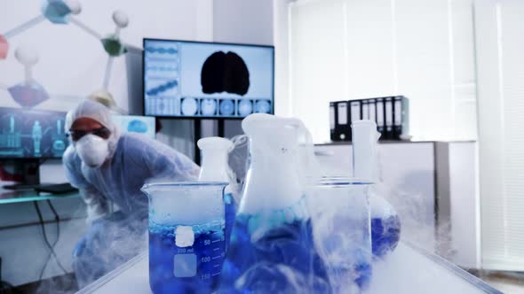Group of Scientist in Coverall Equipment Taking Blue Smoking Liquid From Cart alt