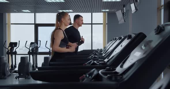A Man And A Girl Go In For Sports In The Gym. Running On A Treadmill 