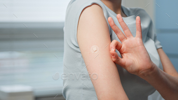 Young woman patient shows OK gesture with fingers near small injection spot on forearm skin / Photodune, Misc