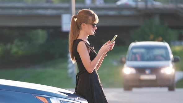 Young Female Driver Standing Near Her Car Talking on Mobile Phone on a City Street in Summer