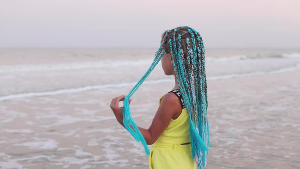 A Girl in a Summer Suit with African Braids Looks at the Sea Horizon While Standing on the Beach