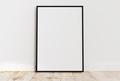Empty thin black frame on light wooden floor with white wall behind it. - PhotoDune Item for Sale
