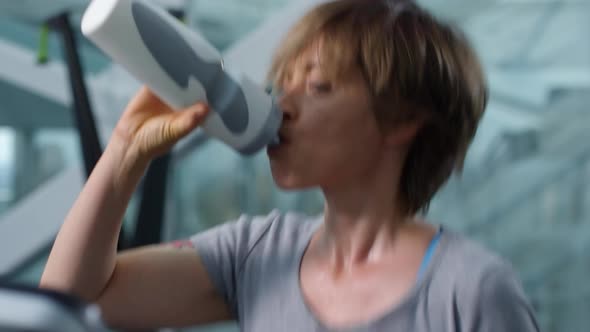 Woman Drinking Water while Running on Treadmill