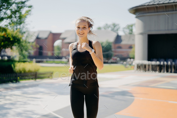 Pleased energetic woman runs quickly on stadium, has healthy fit body listens music / Photodune, Misc