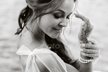 An elegant bride in a white dress, gloves and bare feet is sitting near a waterfall in the Park / Photodune, Misc