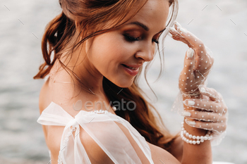 An elegant bride in a white dress, gloves and bare feet is sitting near a waterfall in the Park / Photodune, Misc