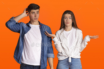 ing or does something wrong. Surprised man scratches back of his head, sad woman spreads her arms to sides isolated on orange background, free space