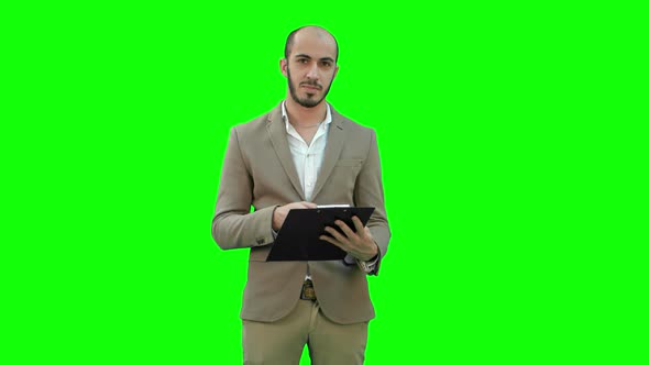 Businessman Holding Clipboard and Presenting Business Report on a Green Screen